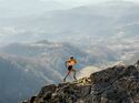 Eine Frau in Laufkleidung läuft einen Bergpass bergauf. Im Hintergrund erstreckt sich ein beeindruckendes Bergpanorama.