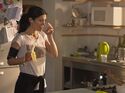 Eine Frau in Sportkleidung steht in der Küche, in der einen Hand eine Banane und in der anderen ein Glas Wasser, aus dem sie gerade trinkt.