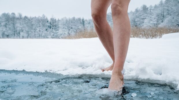 Frau auf dem Weg in einen eiskalten See im Winter. Es sind nur ihre Beine zu sehen.