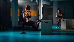 Frau bei einem Bulgarian Split Squat im Gym auf einer Box mit einer Kettlebell in den Händen