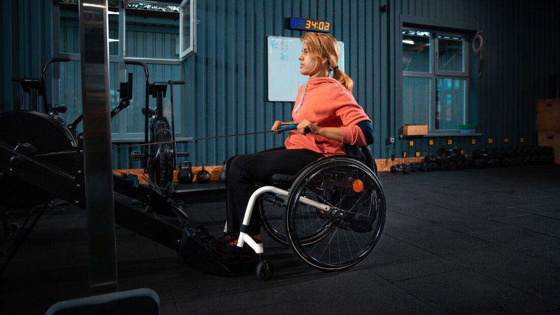 Frau im Rollstuhl trainiert im Fitnessstudio ihren Rücken mit Ruderzügen. 
