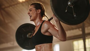 Frau in Sport-BH stemmt Langhantel mit Gewichten