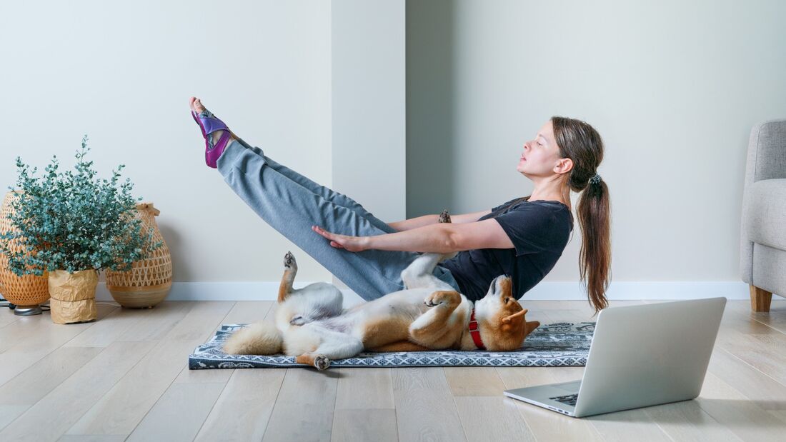 Frau macht auf einer Matte Sport, Hund liegt neben ihr