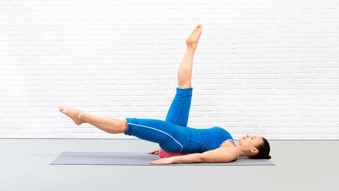 Frau macht mit gestreckten Beinen Kreise in die Luft während ihr unterer Rücken auf dem Pilates-Ball ruht