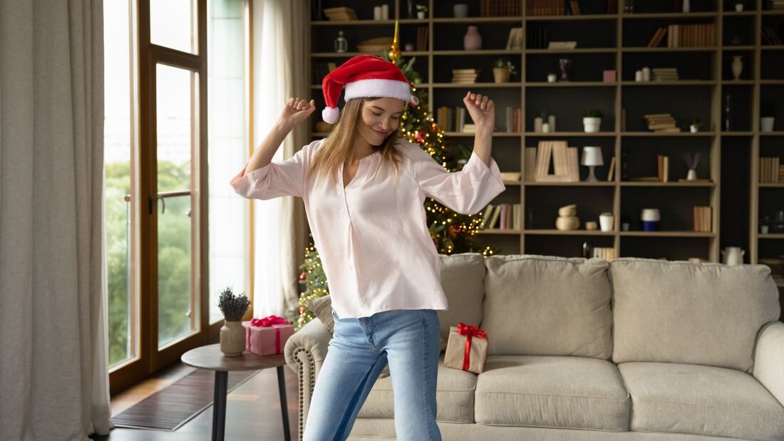Junge Frau mit Weihnachtsmütze tanzt fröhlich vor dem Tannenbaum
