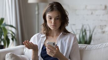 Junge Frau schaut schockiert auf ihr Smartphone-Display