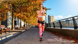 Schwangere Frau joggt in herbstlicher Kulisse